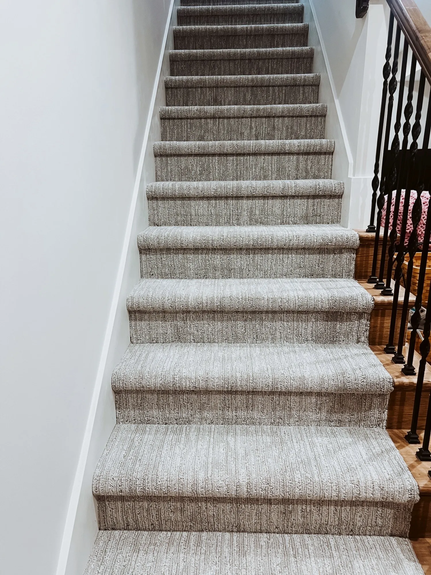 Full run of new carpeted stairs rising between a white stairwell wall and iron balusters, with oak steps at the landing, in a Holden, Missouri whole home remodel