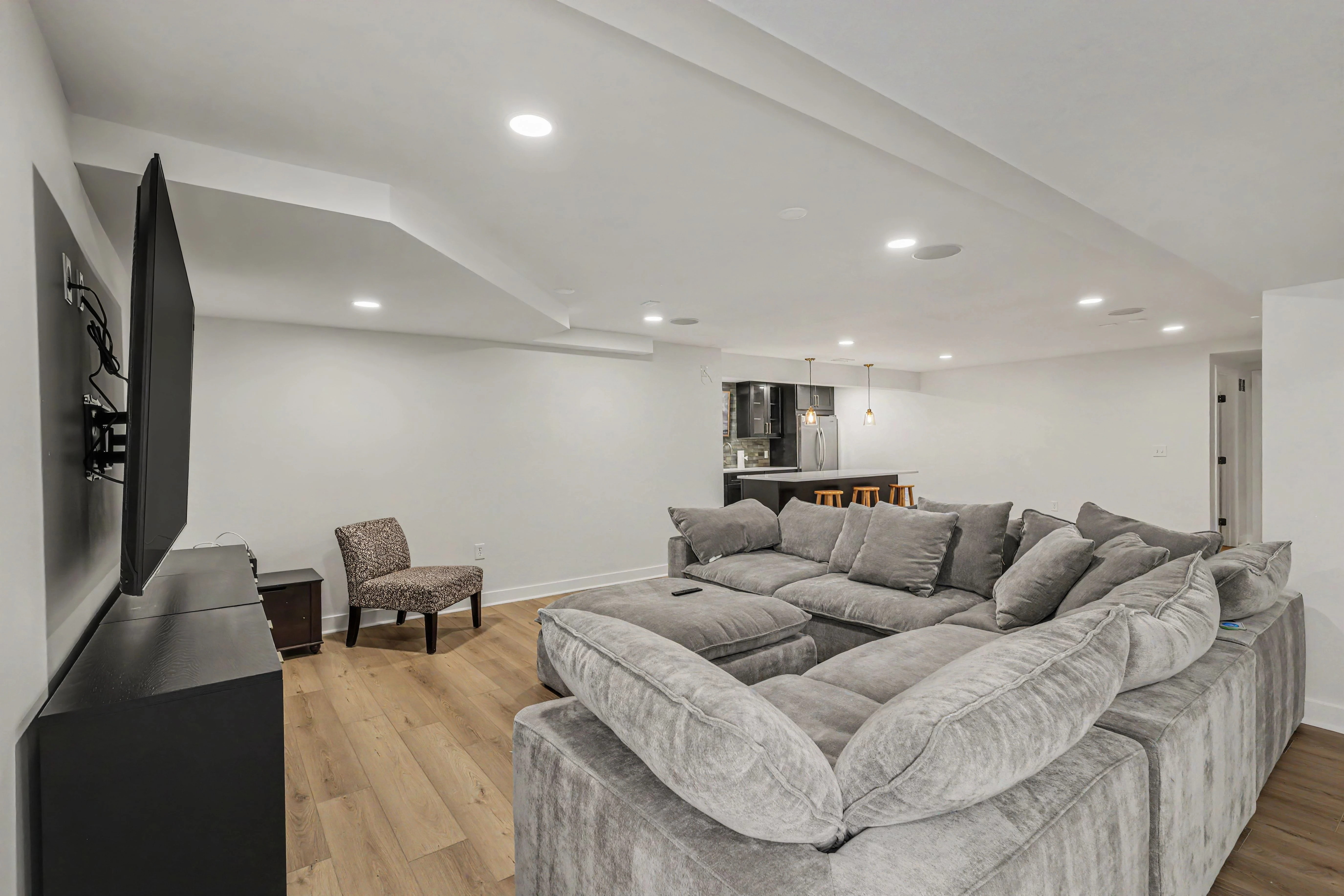 Basement living space with accent chair and kitchenette beyond from a Prairie Village basement remodel