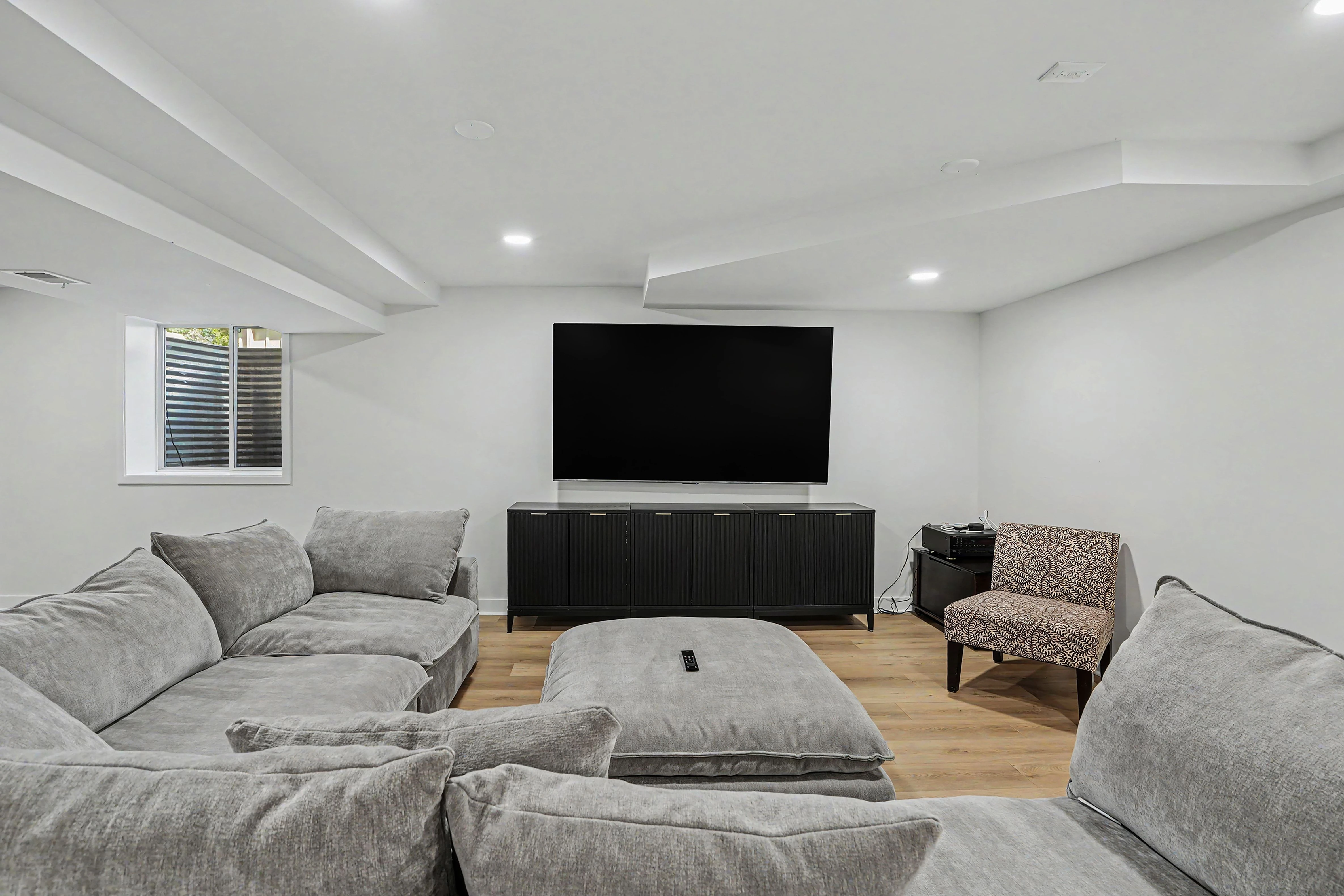 Finished basement family room with wall-mounted TV over a black media console and sectional seating
