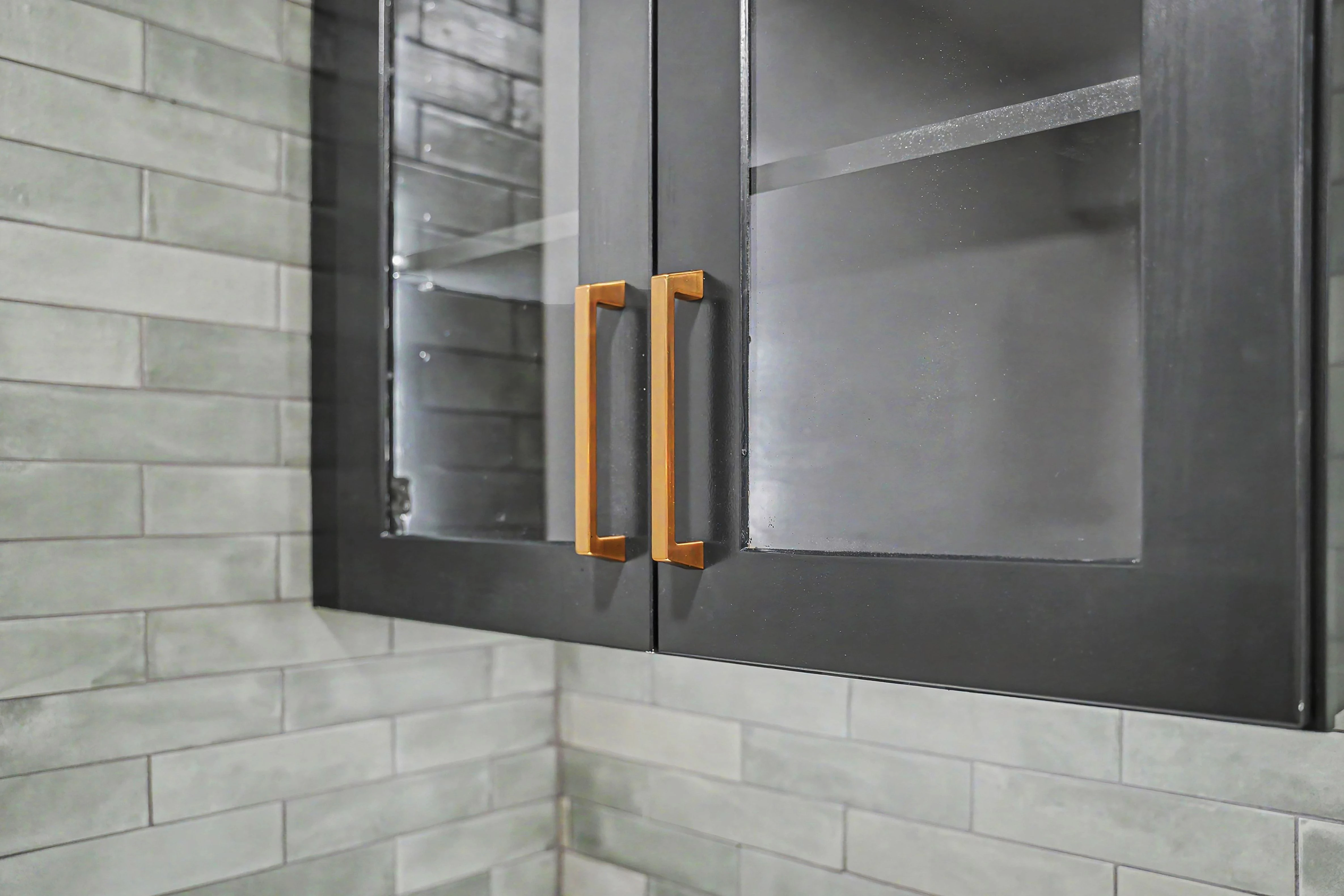 Glass front display cabinets with brass pulls over full height tile in a Prairie Village basement remodel
