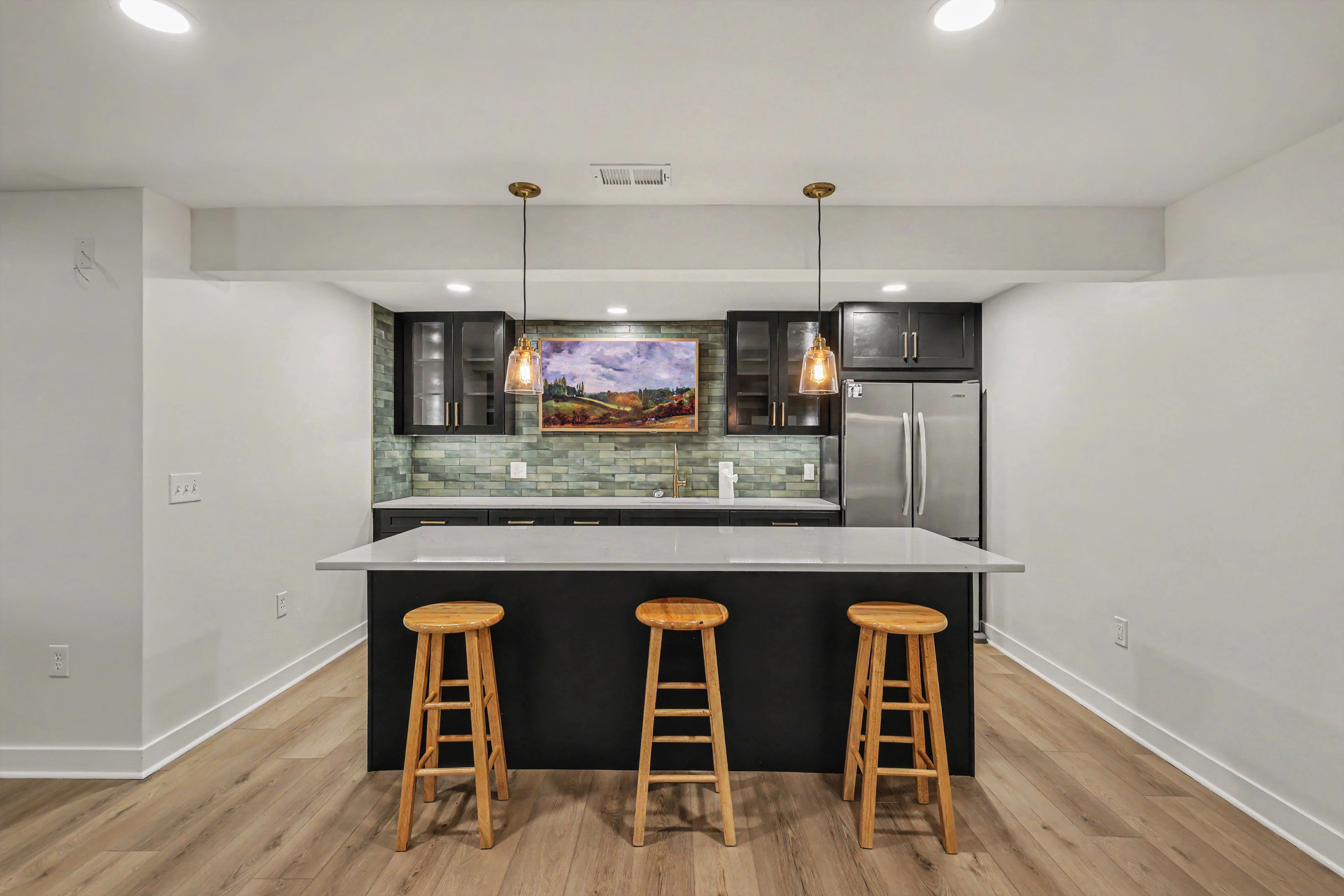 Custom basement kitchenette and bar with black shaker cabinetry, quartz island, and pendant lighting in a Prairie Village basement remodel