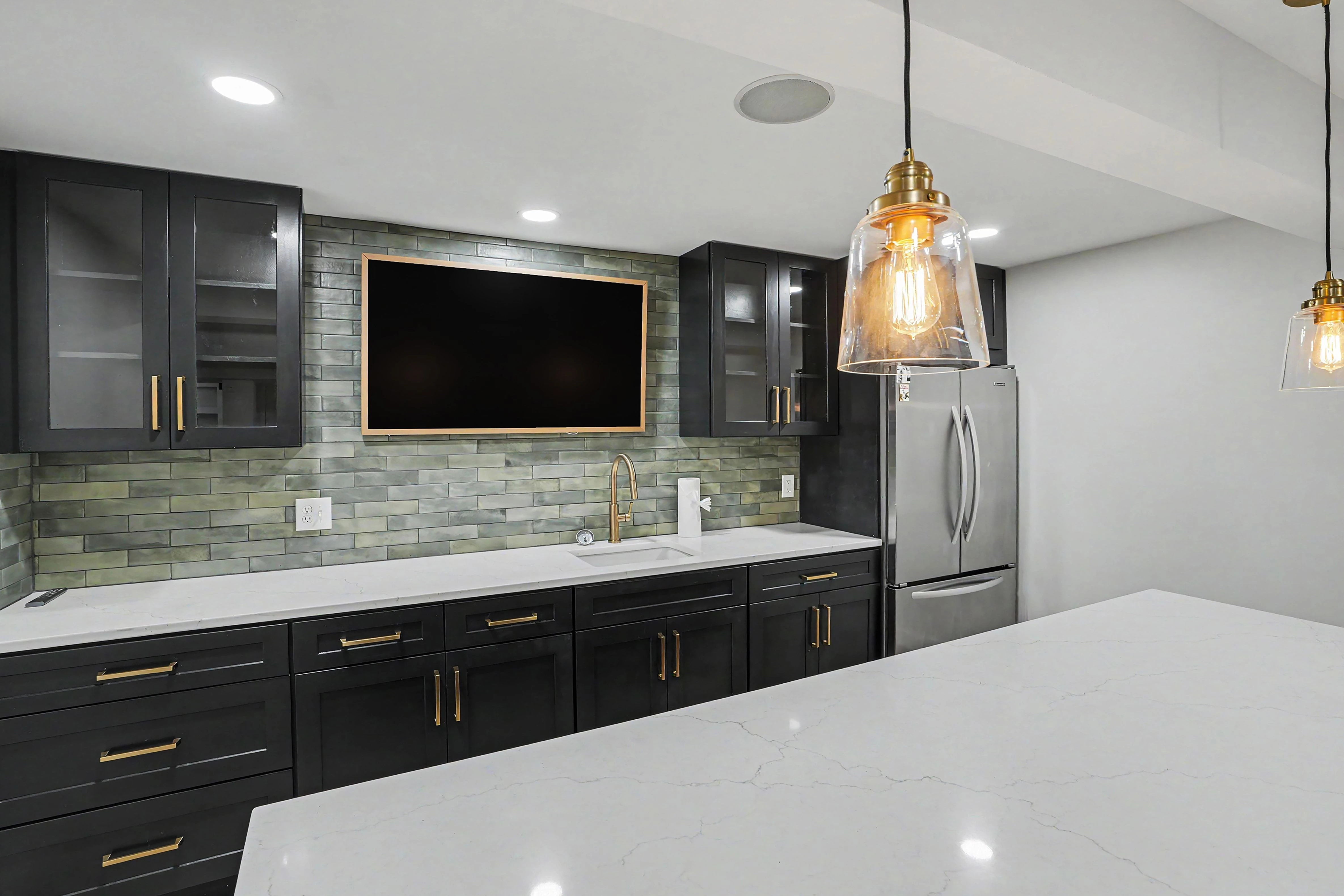Kitchenette sink wall with full height tile backsplash and gold faucet in a Prairie Village basement remodel