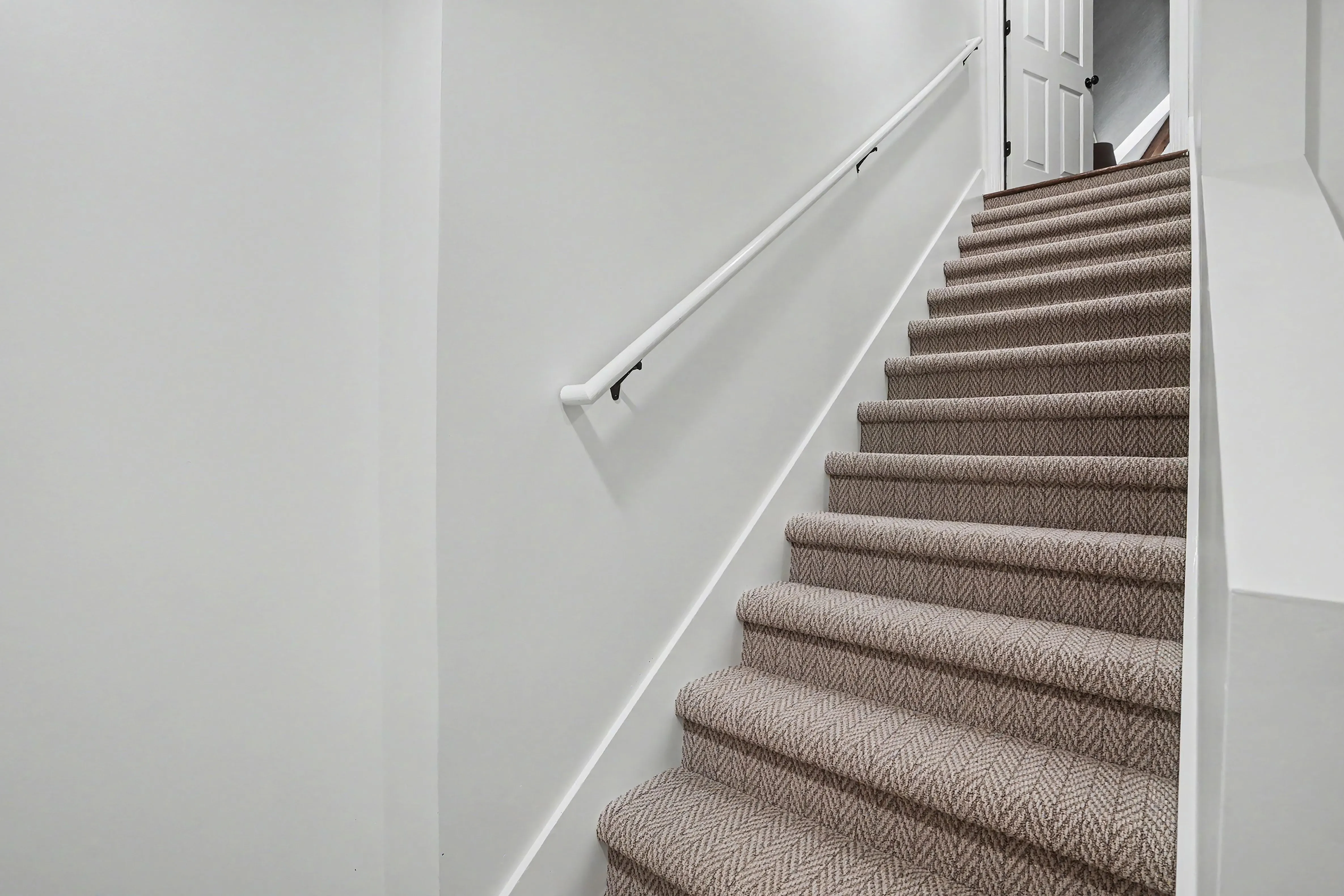 Finished basement stairwell with carpeted stairs and white handrail in a Prairie Village basement remodel