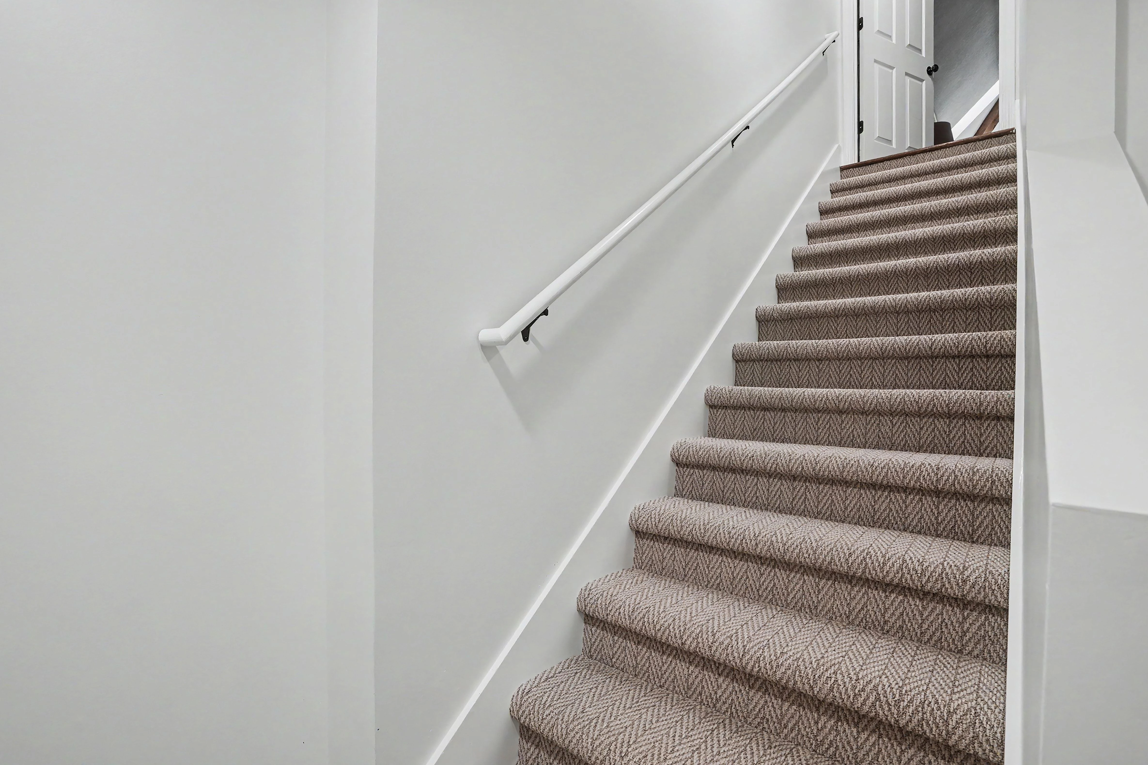 Finished basement stairwell with carpeted stairs and white handrail in a Prairie Village basement remodel