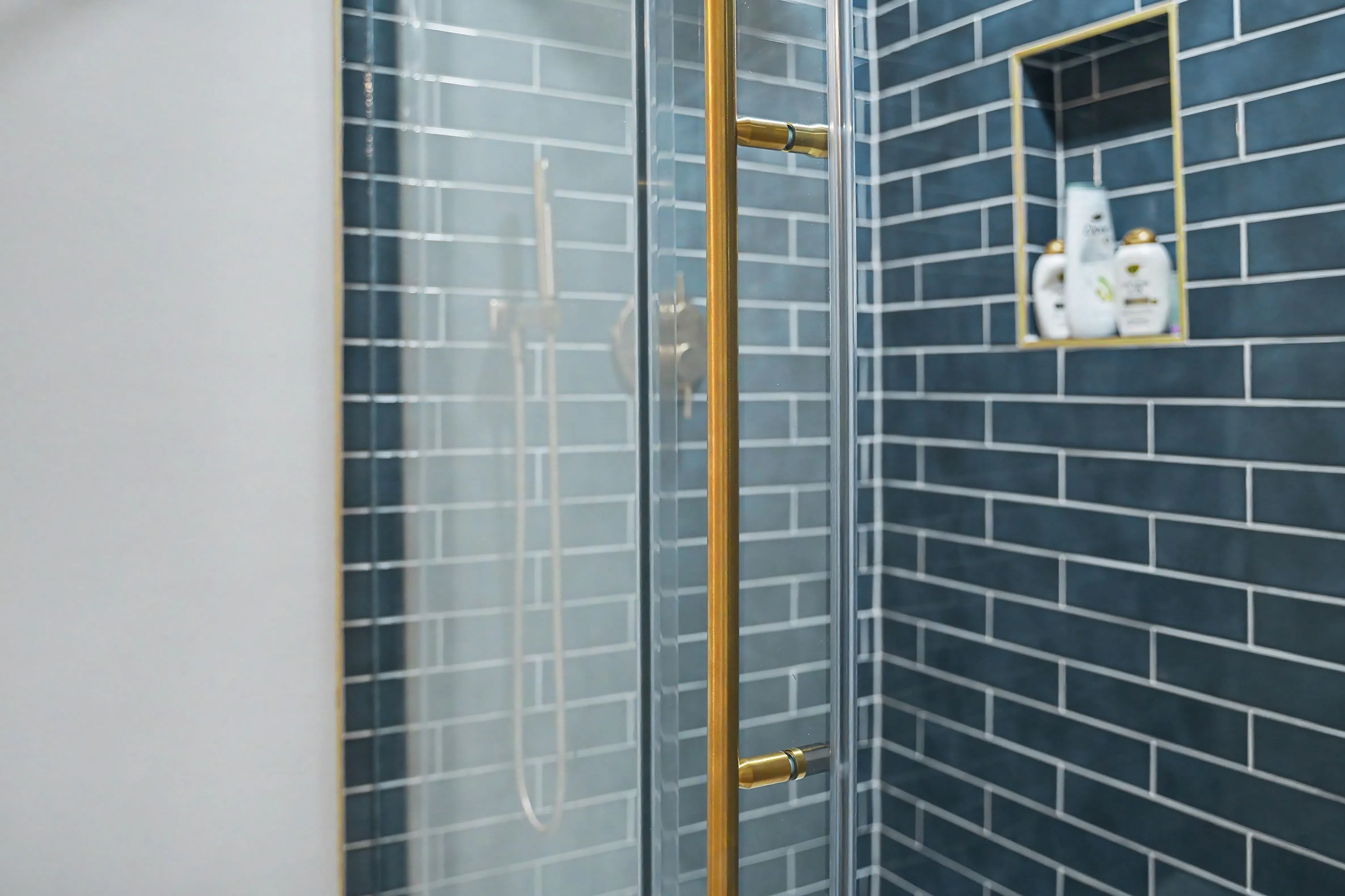 Tiled shower with brass glass door hardware and gold trimmed niche in a Prairie Village basement remodel