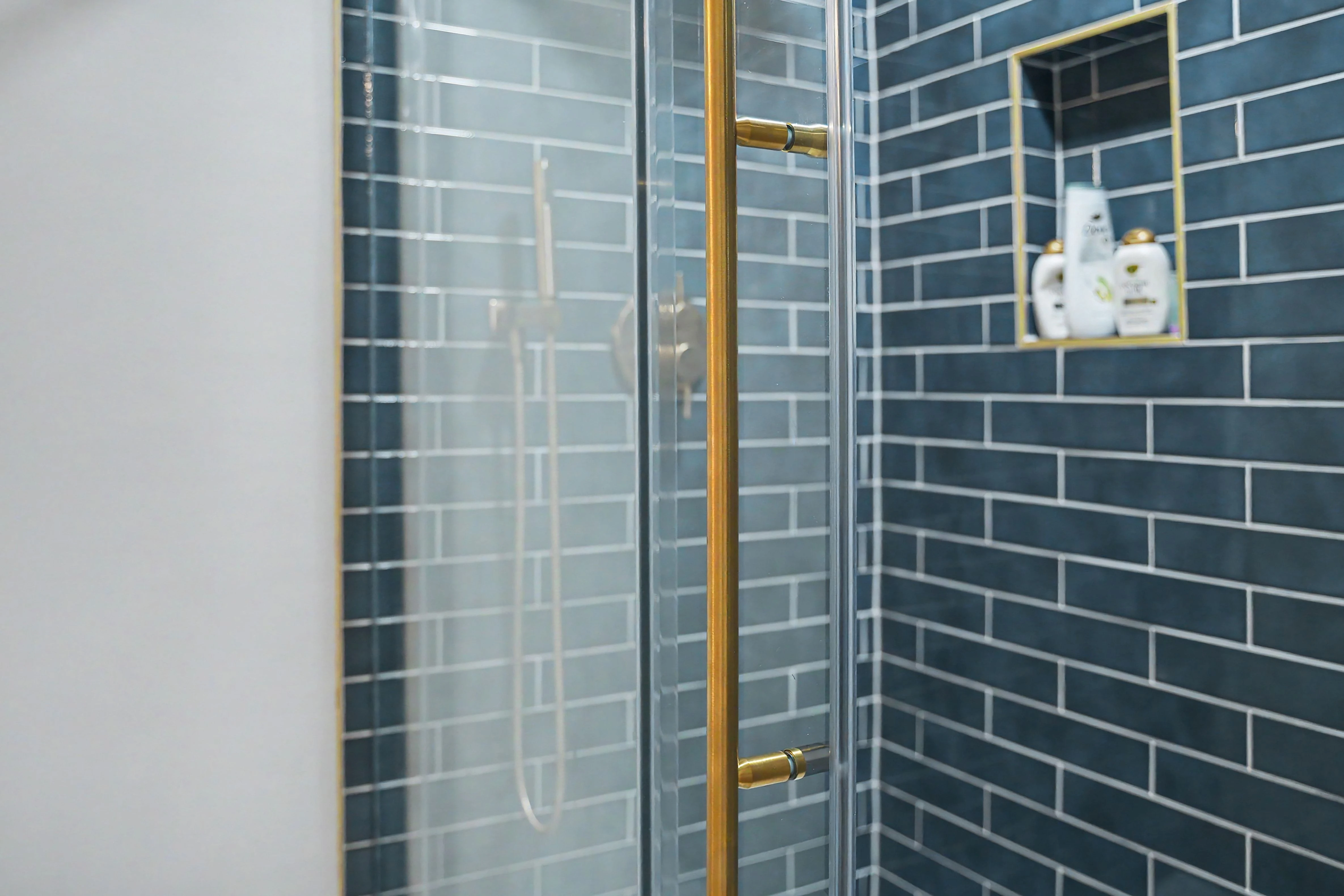 Tiled shower with brass glass door hardware and gold trimmed niche in a Prairie Village basement remodel
