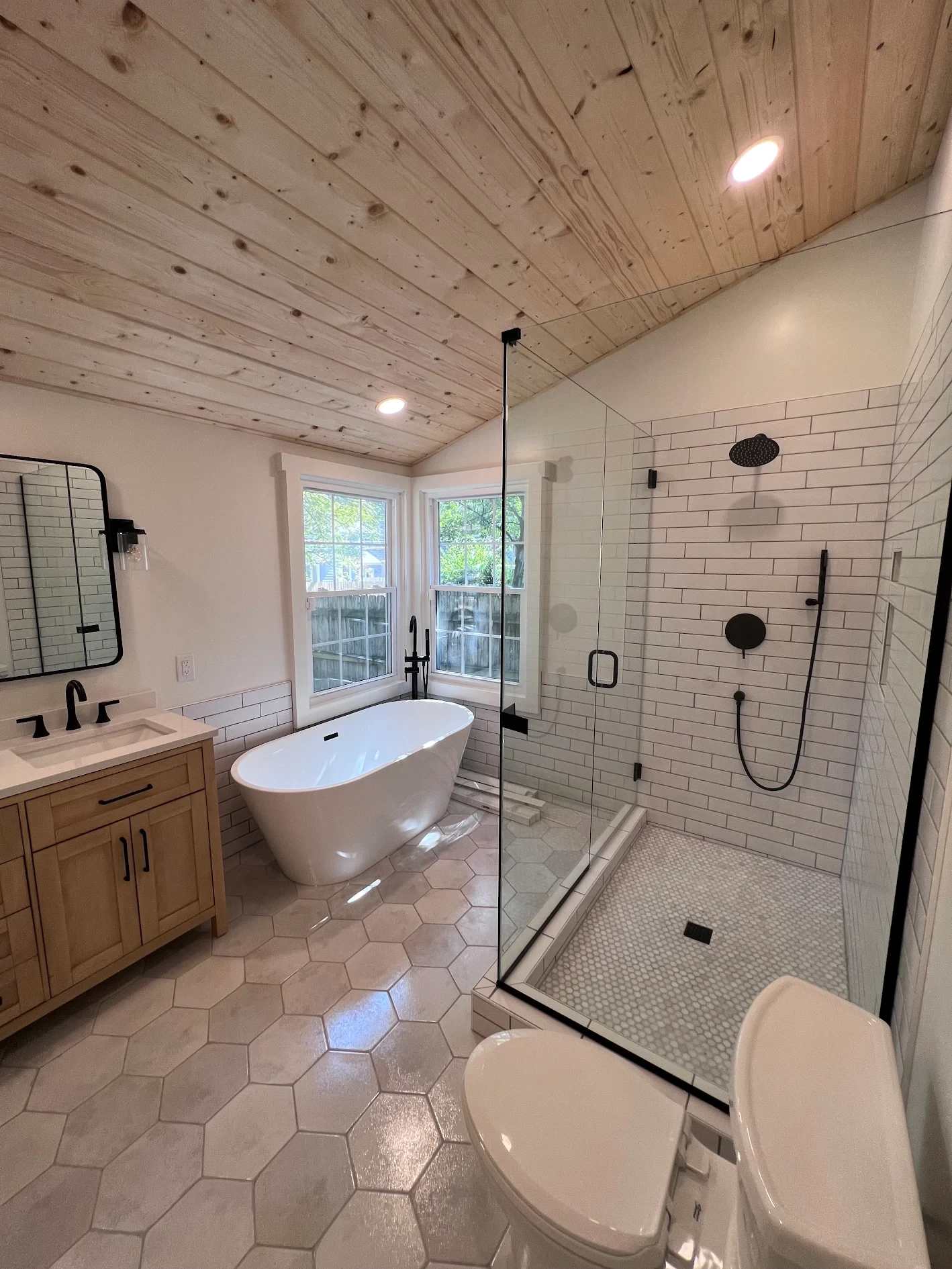 Remodeled primary bathroom with freestanding tub, glass-enclosed subway tile shower, and pine plank ceiling