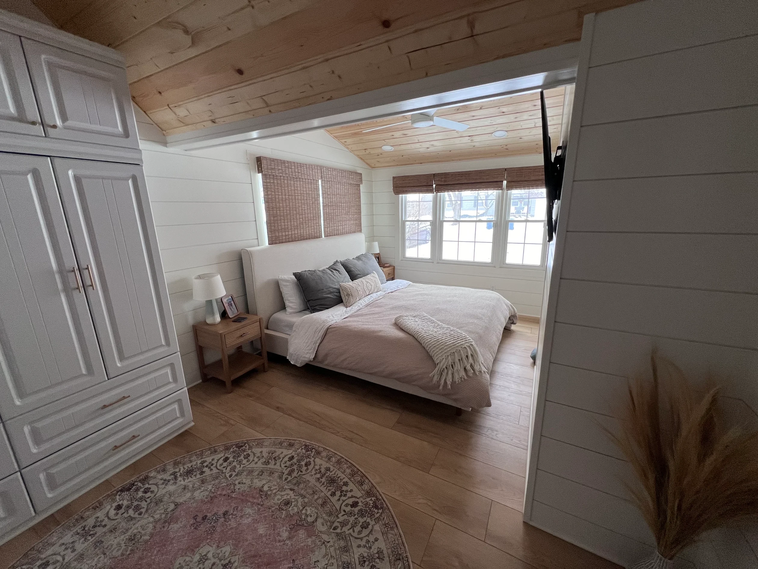 Remodeled primary bedroom with shiplap walls, vaulted pine plank ceiling, and woven window shades